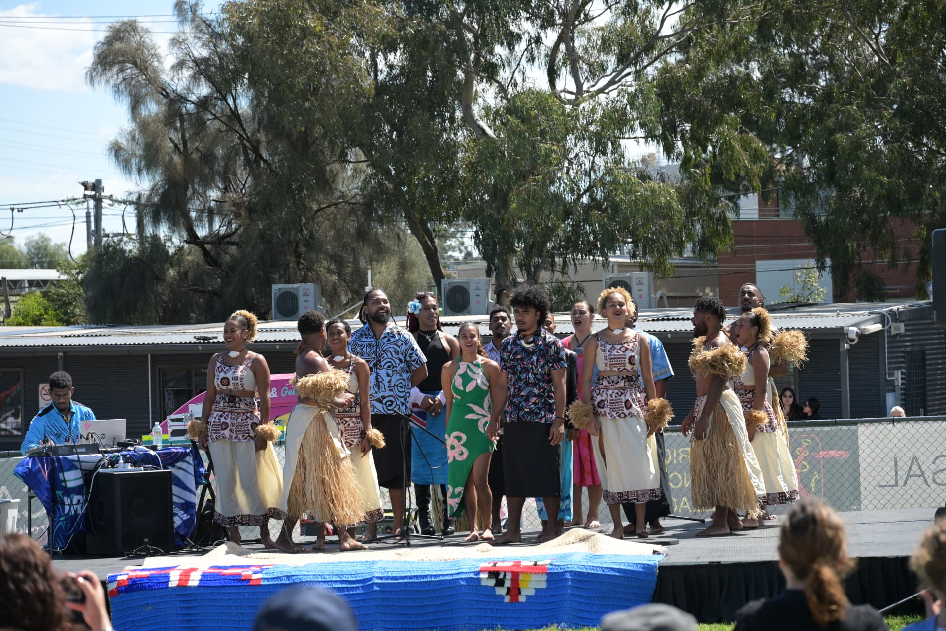 A choir of performers in island wear and grass skirts sings together on the outdoor stage at Fiji Day 2026
