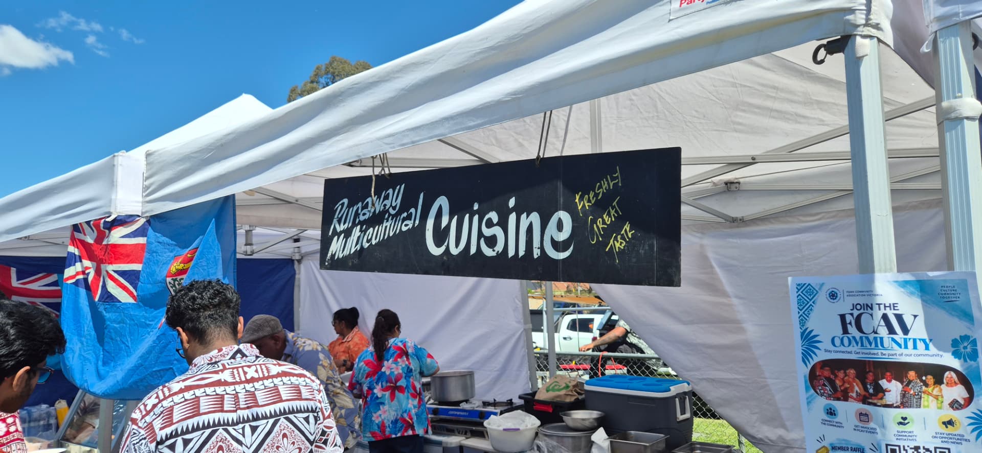 The Runaway Multicultural Cuisine stall under a white marquee with a Fiji flag and the FCAV community banner at Fiji Day 2026
