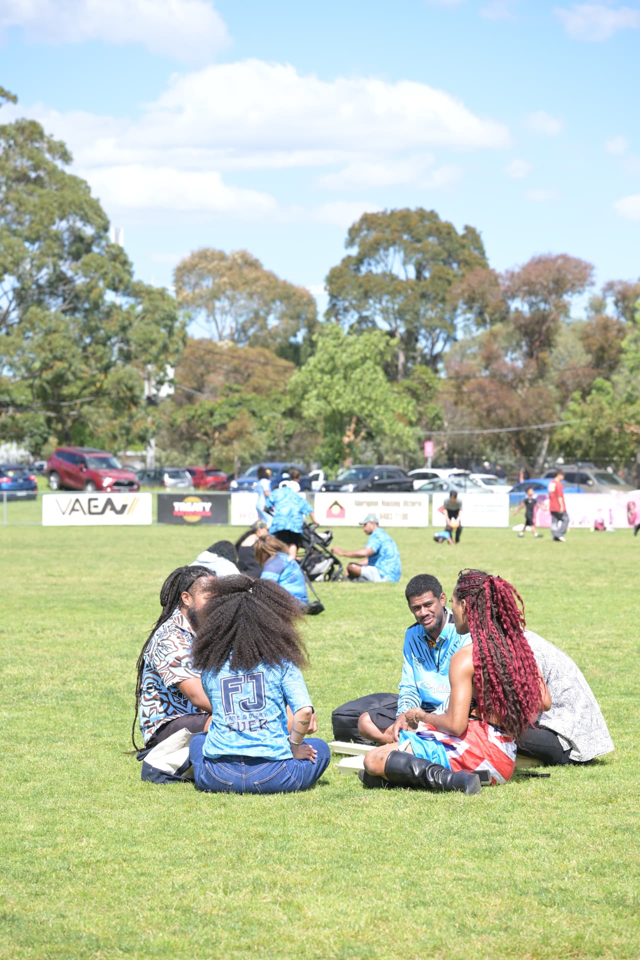 Young adults sit in a circle on the lawn talking while other attendees move across the field at Fiji Day 2026